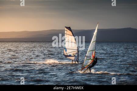Windsurfer Surfing The Wind On Waves In Neusiedl Lake in Austria at Sunset. Recreational Water Sport. Summer Fun Adventure Activity. Stock Photo