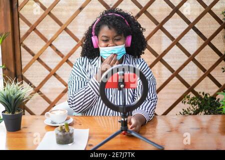 Happy african girl streaming online using phone cam outdoors while wearing mask - Focus on face Stock Photo