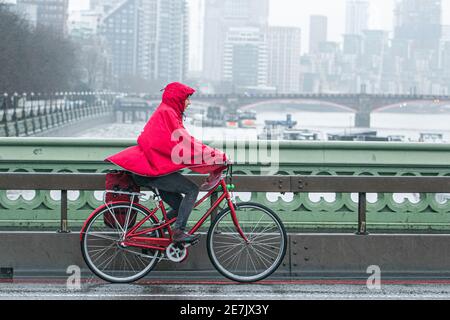 WESTMINSTER LONDON, UK  30 January 2021. A cyclist wearing an anorak rides  on Westminster Bridge on a wet and rainy day. The Met office has issued weather warnings for downpours in the coming days and snow  in northern  parts of the UK. Credit: amer ghazzal/Alamy Live News Stock Photo