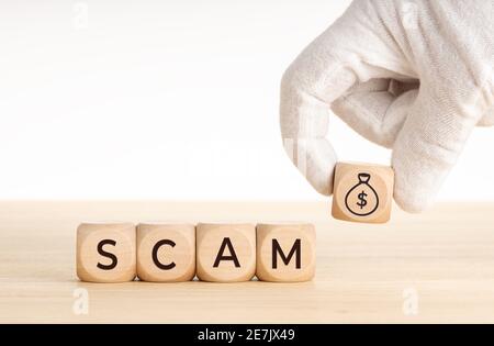 Scam concept. Hand picking a wooden block whit money bag icon and text on wooden dice. Copy space. White background Stock Photo