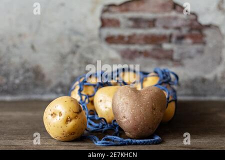 Heart-shaped red potatoes with white potatoes in a blue eco-grid on a wooden background close-up.