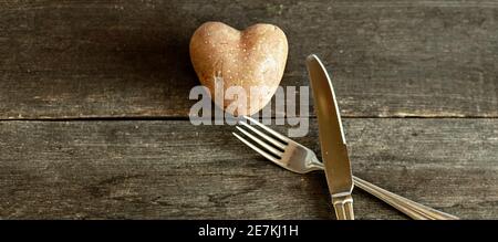 Red potatoes in the shape of a heart on a wooden background with a fork and knife. The concept of agriculture, harvesting, vegetarianism. Valentine's