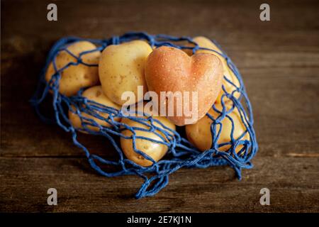 Heart-shaped red potatoes with white potatoes in a blue eco-grid on a wooden background close-up.