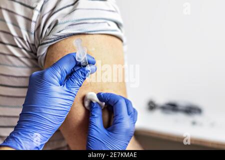 A doctor vaccinates a man against coronavirus at a clinic. Close-up. The concept of vaccination, immunization, prevention against Covid-19 Stock Photo