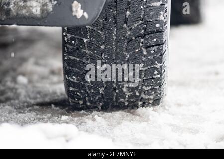 Close up winter studded tires of a car on the road covered by snow and ice driving in extreme cold temperature Stock Photo