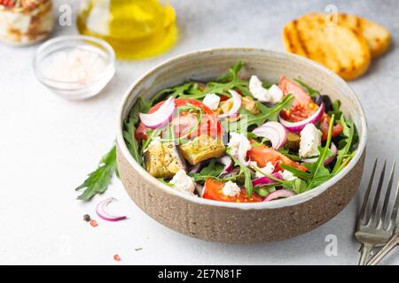 Eggplant salad with tomatoes, arugula and feta cheese in a bowl on white background Stock Photo