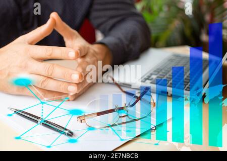 Businessman hands in front of laptop monitor, growth charts and virtual analytics. E-business concept. Stock Photo