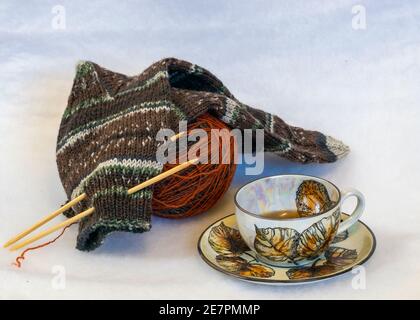 colorful and variegated knit socks with knitting needles, yarn ball and tea cup, handicrafts Stock Photo