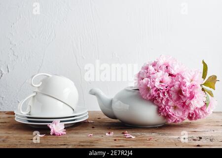 White cups, teapot and pink Japanese cherry blossoms. Spring still life.
