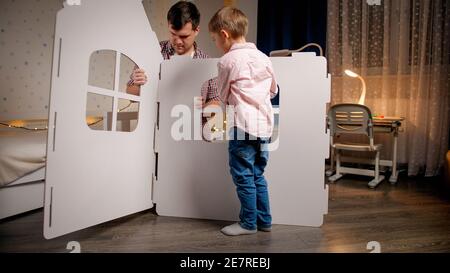 Young father with little son assembling toy cardboard house in children bedroom. Family having good time together. Kids helping parents. Stock Photo