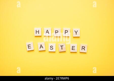 Phrase happy easter made from wooden blocks on a light yellow background Stock Photo