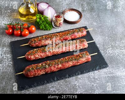 lula kebab raw meat wooden skewer on a black stone surface, spices Stock Photo