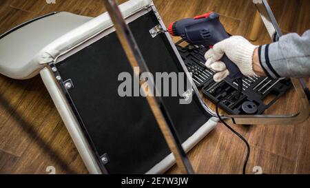 A man repairs furniture using a handheld electric drill to drill a hole to attach the frame. Furniture worker. Stock Photo