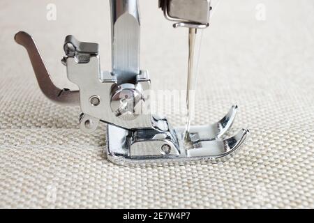 Modern sewing machine presser foot makes a seam on biege fabric. Sewing process Stock Photo