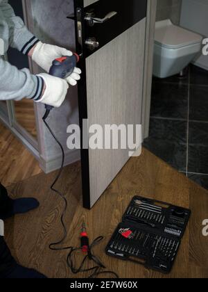A door installer at work, a carpenter drilling a door lock, a handyman repairing an interior door. Home worker. Stock Photo