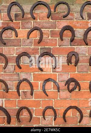 Horseshoe background, rows of old horseshoes on a brick wall, UK Stock Photo