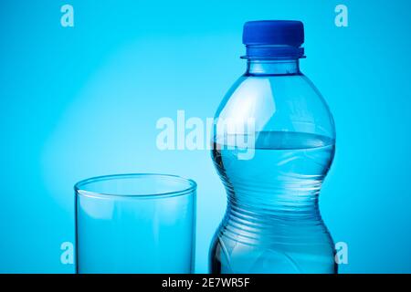 A bottle of mineral water and an empty glass on a blue background. Stock Photo