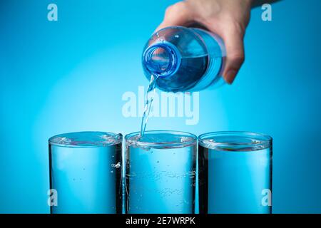 Three clear glasses are filled with water from a bottle on a blue background. Stock Photo