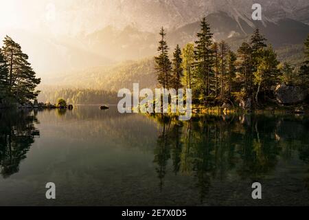 Warm sunrise during a calm, peaceful morning on Eibsee / Lake Eib in Bavaria, Germany, in front of Zugspitze, with clean reflections in the water. Stock Photo