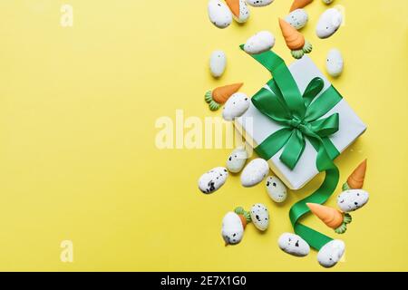Flying quail eggs and sweet carrot with gift box with green ribbon on yellow trend color background. Spring Happy Easter holiday Greeting card. Top vi Stock Photo