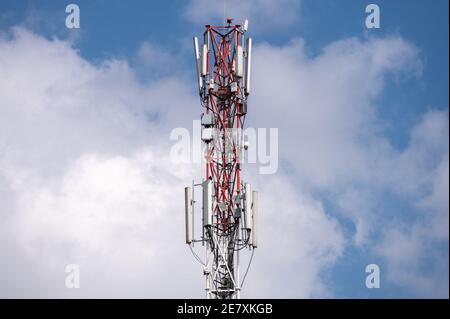 A cell phone or mobile phone antenna mast against a sunny cloudy sky Stock Photo
