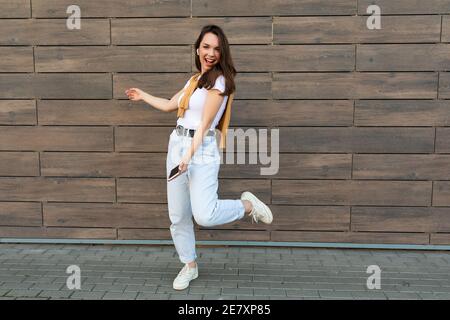 Full length body size photo of pretty brunet young happy woman wearing casual clothes and listening to music via wireless earphones standing in the