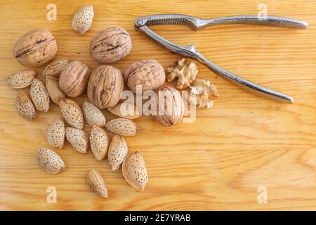 Tasty walnuts, almond and metal nutcracker on a wooden background. Stock Photo
