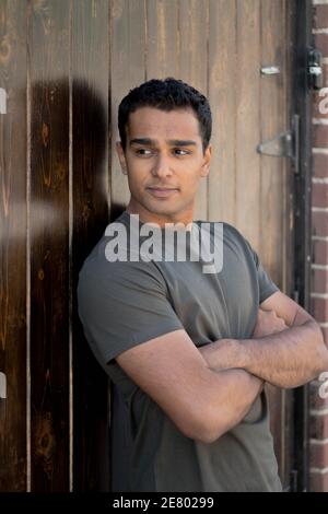 Man looking down a corridor while leaning on a door in a relaxed pose Stock Photo