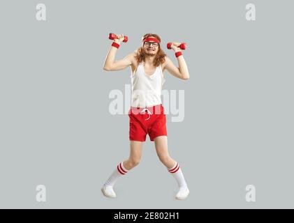 Funny tired skinny man doing exercise with gym dumbbells isolated on gray background Stock Photo