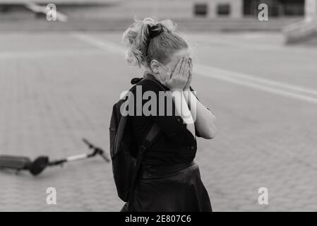 Girl sitting crying after she fell while riding her scooter at city street Stock Photo