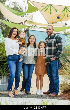 A family of five with two girls and a baby boy standing outside in a downtown park area Stock Photo