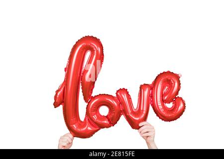 Red golden word LOVE made of inflatable balloons in hands isolated on white background. Red foil balloon letters, concept of romance, Valentine's Day Stock Photo