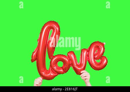 Red golden word LOVE made of inflatable balloons in hands isolated on green screen. Red foil balloon letters, concept of romance, Valentine's Day Stock Photo