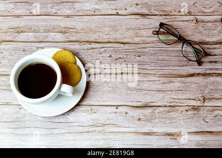 A coffee and a pair of glasses laid on a wooden table shot from above Stock Photo