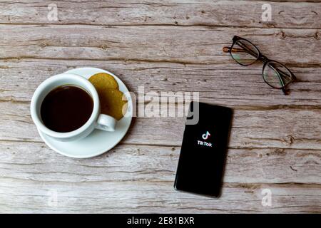 A Mobile phone or cell phone laid on a wooden table with the TikTok app opening also a coffee and glasses Stock Photo