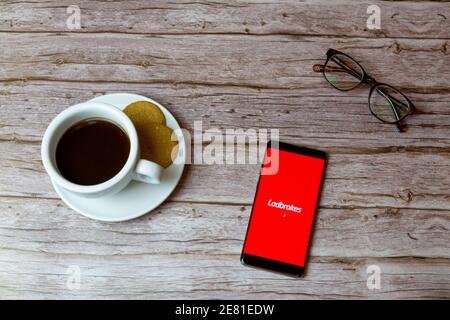 A Mobile phone or cell phone laid on a wooden table with the Ladbrokes app opening also a coffee and glasses Stock Photo