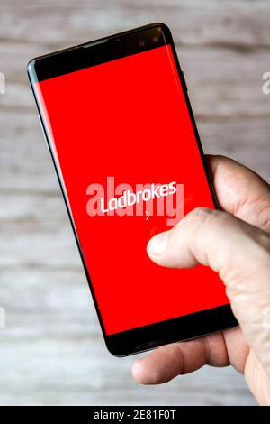 A hand holding a mobile phone or cell phone with the Ladbrokes bookmaking app open on screen Stock Photo