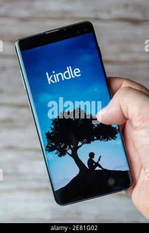 A hand holding a mobile phone or cell phone with the Kindle app open on screen Stock Photo