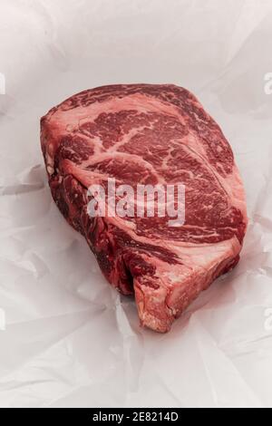 A raw New York strip Ribeye steak thick steak on paper that its wrapped in when bought fresh from a store. Stock Photo