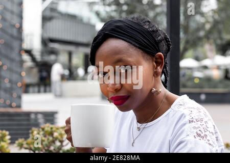 Close up of African lady in white holding cup of coffee or tea, afe exterior, enjoying hot drink Stock Photo