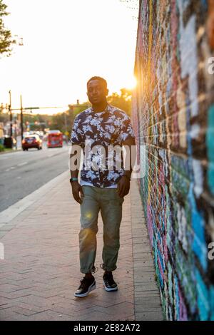 A Black man walks past a colorful mural in an urban setting. Stock Photo
