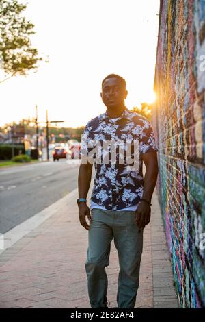 A Black man walks past a colorful mural in an urban setting. Stock Photo