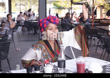 Fashionable African lady wearing a doek or head scarf waving at a friend Stock Photo