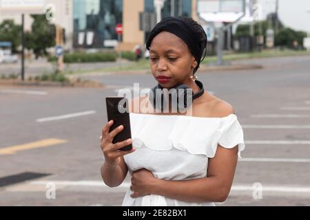 Unsmiling African woman taking a selfie with a smartphone with black headphones. Stock Photo