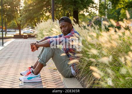 A Black man sits on the curb in an setting. Stock Photo