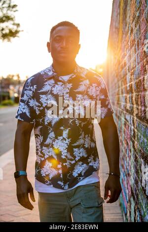 A Black man walks past a colorful mural in an urban setting as the sun goes down behind him. Stock Photo