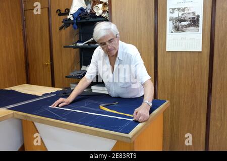 Bari, Italy - July 08, 2013: in a workshop of the old town of Bari, an elderly tailor is tracing with the chalk the pattern on the cloth to be able to Stock Photo