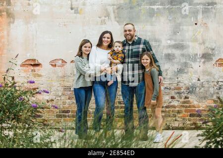 A family of five with two girls and a baby boy standing by an urban old brick wall Stock Photo