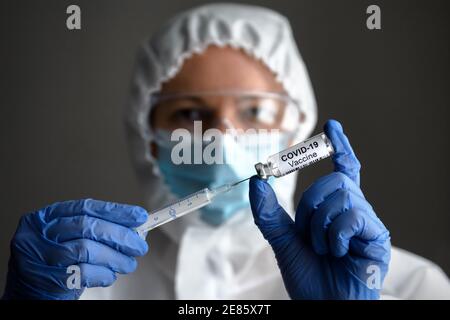 COVID-19 vaccine in doctor’s hands, nurse in medical PPE suit holds syringe and bottle with vaccine for coronavirus cure. Concept of corona virus trea Stock Photo