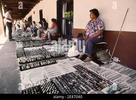 Native Americans and other local artisans sit in the shade behind their sidewalk displays of handmade jewelry awaiting tourists shopping for souvenirs in Old Town Plaza in Albuquerque, the capital of New Mexico, USA. This informal outdoor market on the east side of the plaza lines the covered patio in front of historic La Placita Dining Rooms that has been serving traditional New Mexican food since the 1930s.